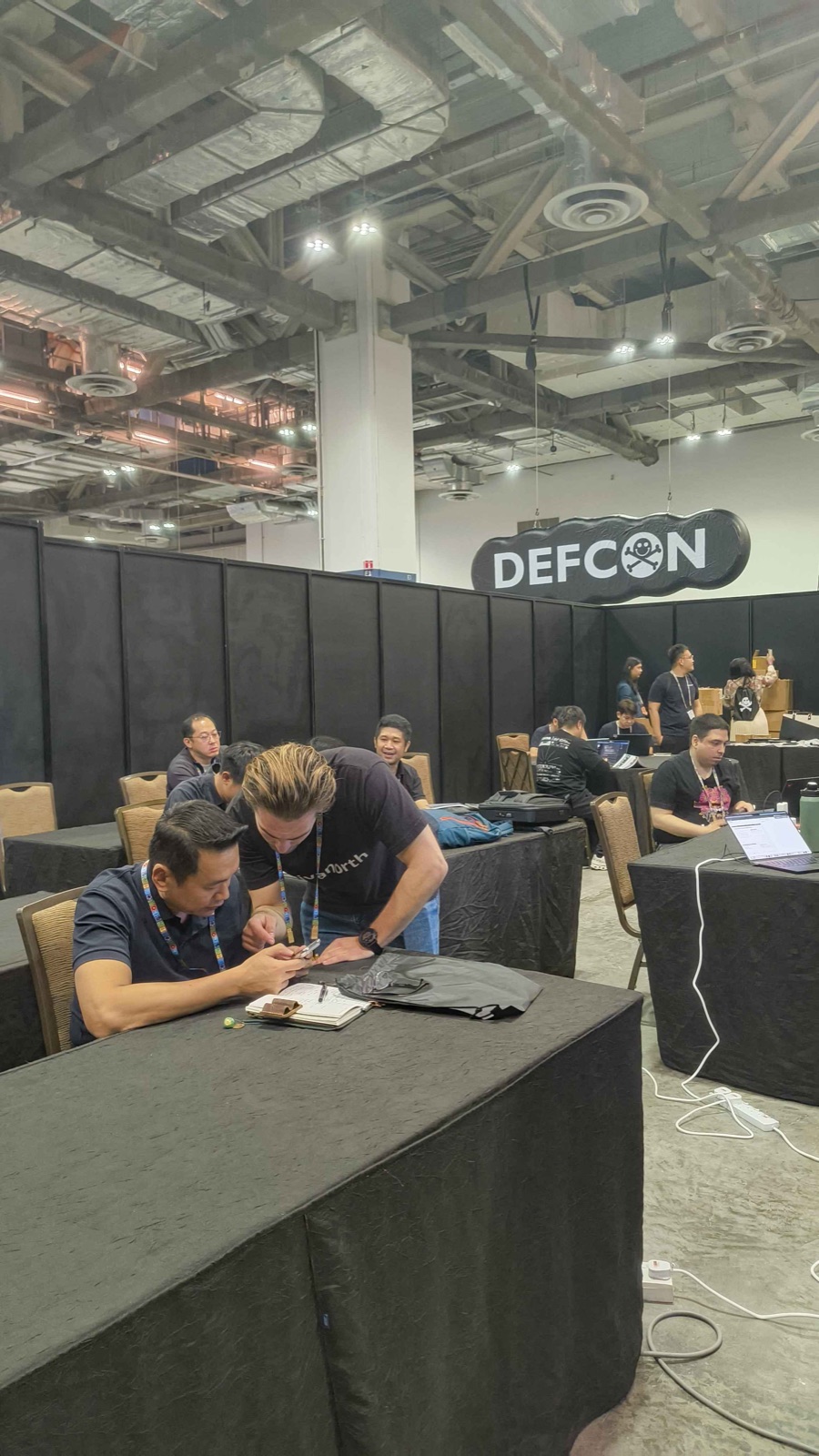 Helping a participant at a desk with the DEF CON logo visible in the background.